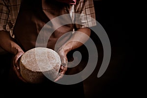 Handsome cheesemaker is checking cheeses in his workshop storage.