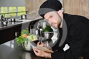 handsome chef writing down new recipe to notebook at restaurant kitchen