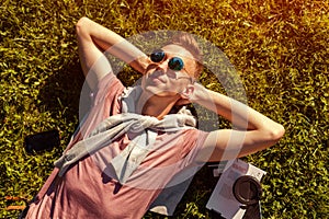 Handsome college man chilling in spring campus park. Happy guy student lying on grass with his phone and coffee beside