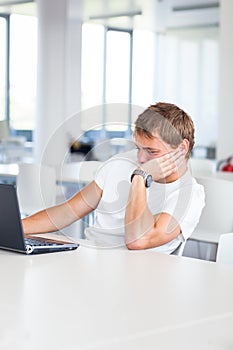 Handsome college student with laptop computer in university library/study room