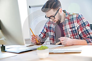 Handsome concentrated man working with blueprint using ruler and pencil