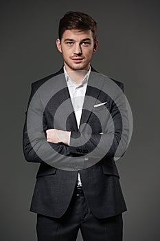 Handsome confident businessman in black suit standing with arms crossed