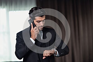 Handsome confident businessman delayed checking the time in the watch while he is making a telephone call with his mobile phone