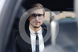 Handsome confident businessman in suit talking on smart phone and working using laptop while sitting in the car