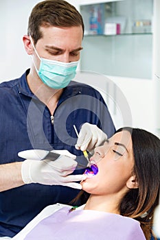 Handsome confident dentist whitening tooth to female patient on dental chair in dental clinic