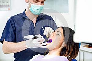 Handsome confident dentist whitening tooth to female patient on dental chair in dental clinic