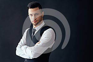 Handsome confident man in elegant suit with crossed arms on black background