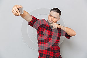 Handsome confident man in plaid shirt taking selfie on smartphone