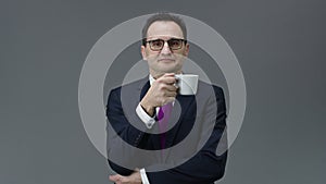 Handsome confident middle aged man holding cup of coffee and looks at camera
