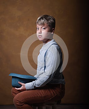 Handsome confident young boy with hat in hand on dark background