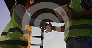 Handsome construction man and woman workers in protective helmets and vests are shaking hands while working in the
