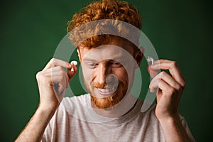 Handsome curly redhead man in white t-shirt insert earphones in