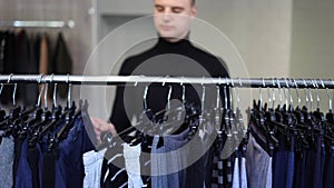 Handsome customer in black golf try to fing some clother for new season. Autumn and winter clothes. Camera moves from