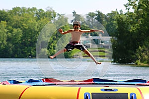 Handsome cute boy jumping at a water trampoline floating in a lake in Michigan during summer.