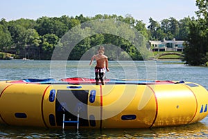 Handsome cute boy jumping at a water trampoline floating in a lake in Michigan during summer.