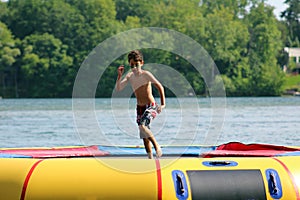 Handsome cute boy jumping at a water trampoline floating in a lake in Michigan during summer.