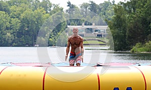 Handsome cute man jumping at a water trampoline floating in a lake in Michigan during summer.