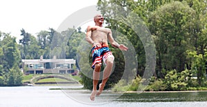 Handsome cute man jumping at a water trampoline floating in a lake in Michigan during summer.