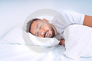 Handsome cute man sleeping in the bed with white beddings. Man lying on the pillow and enjoying good healthy sleep