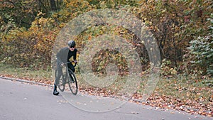 Handsome cyclist starting to ride on road bike in autumn city park. Triathlete pedalling on road bicycle. Male sportive guy in bla