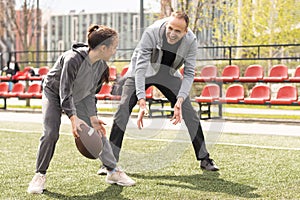 Handsome dad with his little cute daughter are having fun and playing American football on green grassy lawn