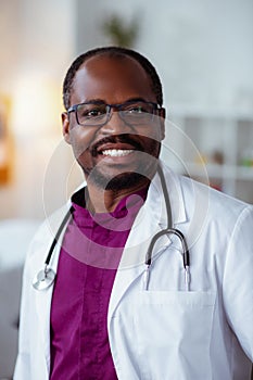 Handsome dark-skinned doctor smiling after good day at work