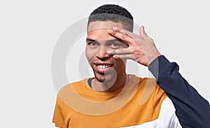 Handsome dark skinned man hiding his face with palm and show his eye. Studio portrait of young male covering his face by hand