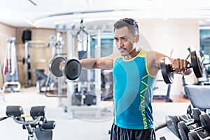 Handsome determined young man exercising with dumbbells in a modern fitness club