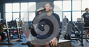 handsome disabled athlete man with prosthetic legs sitting at gym drinking water