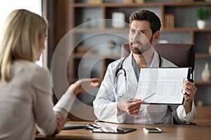 Handsome Doctor Man Showing Medical Test Results To Female Patient In Office