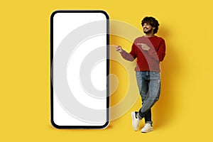 Handsome eastern guy pointing at huge cell phone, mockup