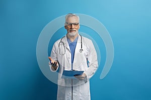 Handsome elderly doctor consulting patient, taking anamnesis, blue background