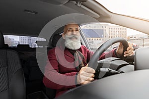 Handsome elderly grey-haired man sitting inside new car, traveling alone