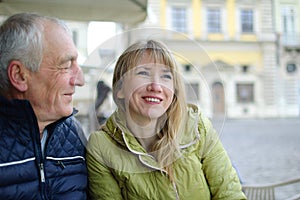 Handsome elderly man is embracing his young blonde wife spending time together outdoors in the ancient city during early