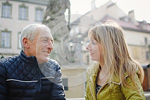 Handsome elderly man is embracing his young blonde wife spending time together outdoors in the ancient city during early