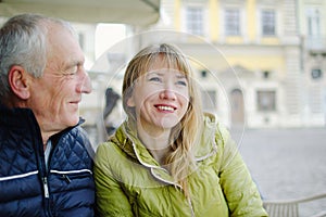 Handsome elderly man is embracing his young blonde wife spending time together outdoors in the ancient city during early