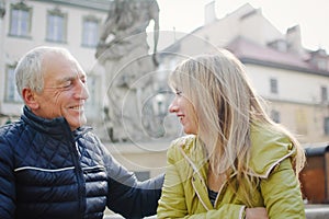 Handsome elderly man is embracing his young blonde wife spending time together outdoors in the ancient city during early