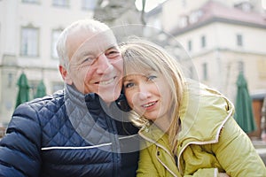 Handsome elderly man is embracing his young blonde wife spending time together outdoors in the ancient city during early