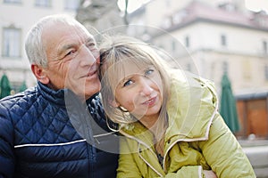 Handsome elderly man is embracing his young blonde wife spending time together outdoors in the ancient city during early