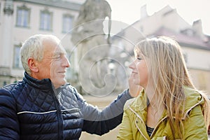 Handsome elderly man is embracing his young blonde wife spending time together outdoors in the ancient city during early