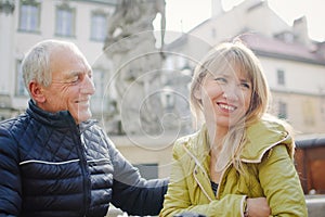 Handsome elderly man is embracing his young blonde wife spending time together outdoors in the ancient city during early