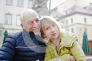 Handsome elderly man is embracing his young blonde wife spending time together outdoors in the ancient city during early