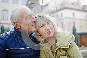 Handsome elderly man is embracing his young blonde wife spending time together outdoors in the ancient city during early