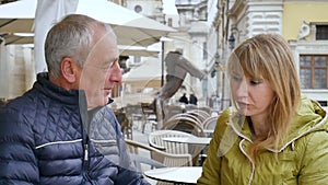 Handsome elderly man is embracing his young blonde wife spending time together outdoors in the ancient city during early