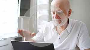 Handsome elderly senior man receiving very bad news on his laptop computer screen and upset