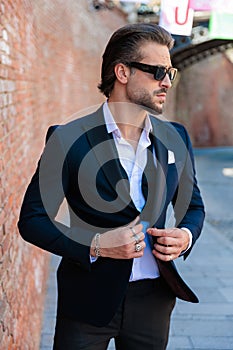 handsome elegant man with glasses looking to side and buttoning suit