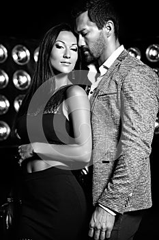 Handsome elegant man in suit with beautiful woman posing on black studio lights background