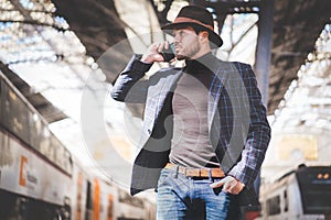 Handsome elegant young hispanic man holding smart phone in his hand and calling while he standing at the railway