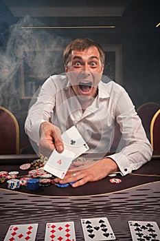 Handsome emotional man is playing poker sitting at the table in casino.