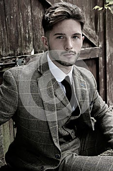 Handsome English gangster dressed in waistcoat and jacket sitting and looking at camera